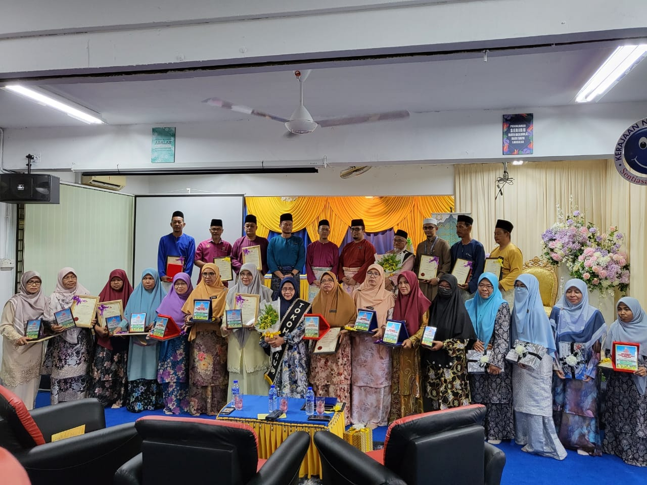 Pelajar tahfiz dan guru bergambar bersama dalam program atau majlis sekolah di dalam dewan.