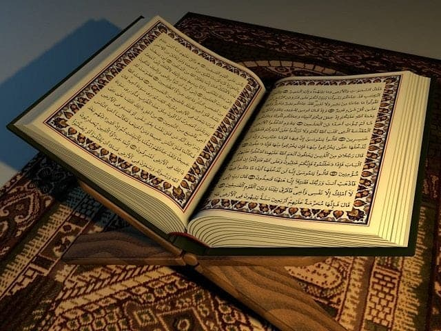 Al-Quran terbuka di atas rehal kayu dengan pencahayaan lembut di atas hamparan sejadah.