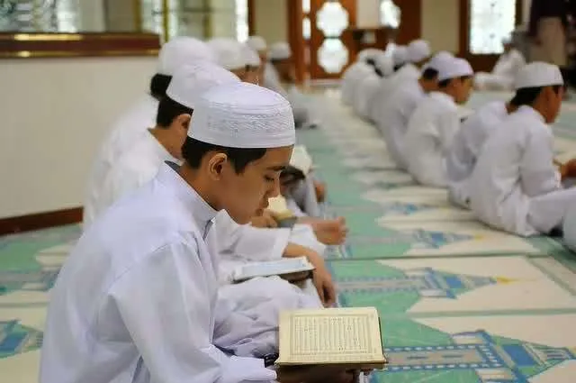 Pelajar tahfiz lelaki sedang membaca dan menghafaz al-Quran di dalam masjid.