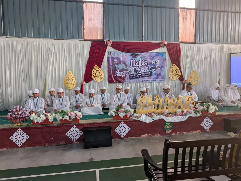 Pelajar tahfiz lelaki sedang menghadiri majlis khatam al-Quran di atas pentas dengan dekorasi bertema Islamik.
