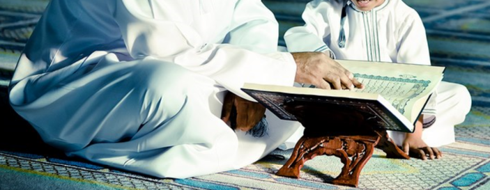 Guru dan pelajar sedang membaca al-Quran bersama di atas rehal kayu di dalam masjid.