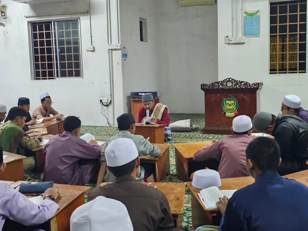 Pelajar tahfiz lelaki menghadiri sesi pengajian al-Quran dan hadis bersama guru di dalam kelas malam.