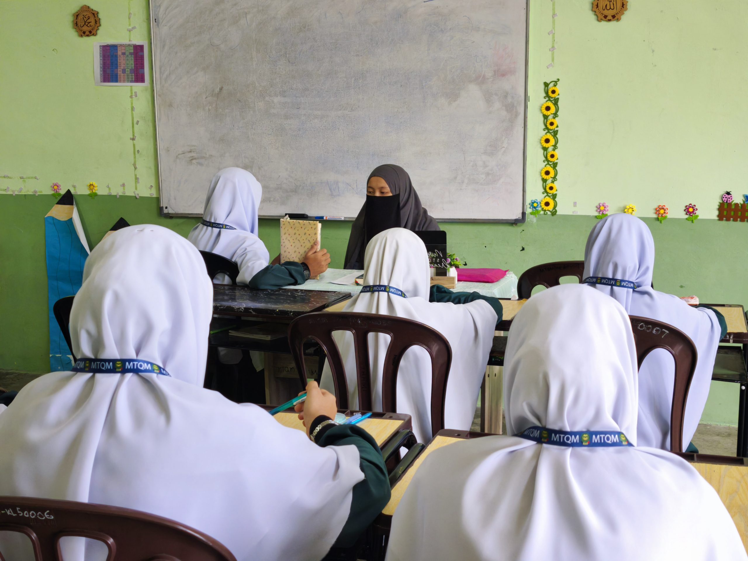 Pelajar tahfiz perempuan sedang mengikuti sesi pembelajaran al-Quran bersama guru di dalam kelas.